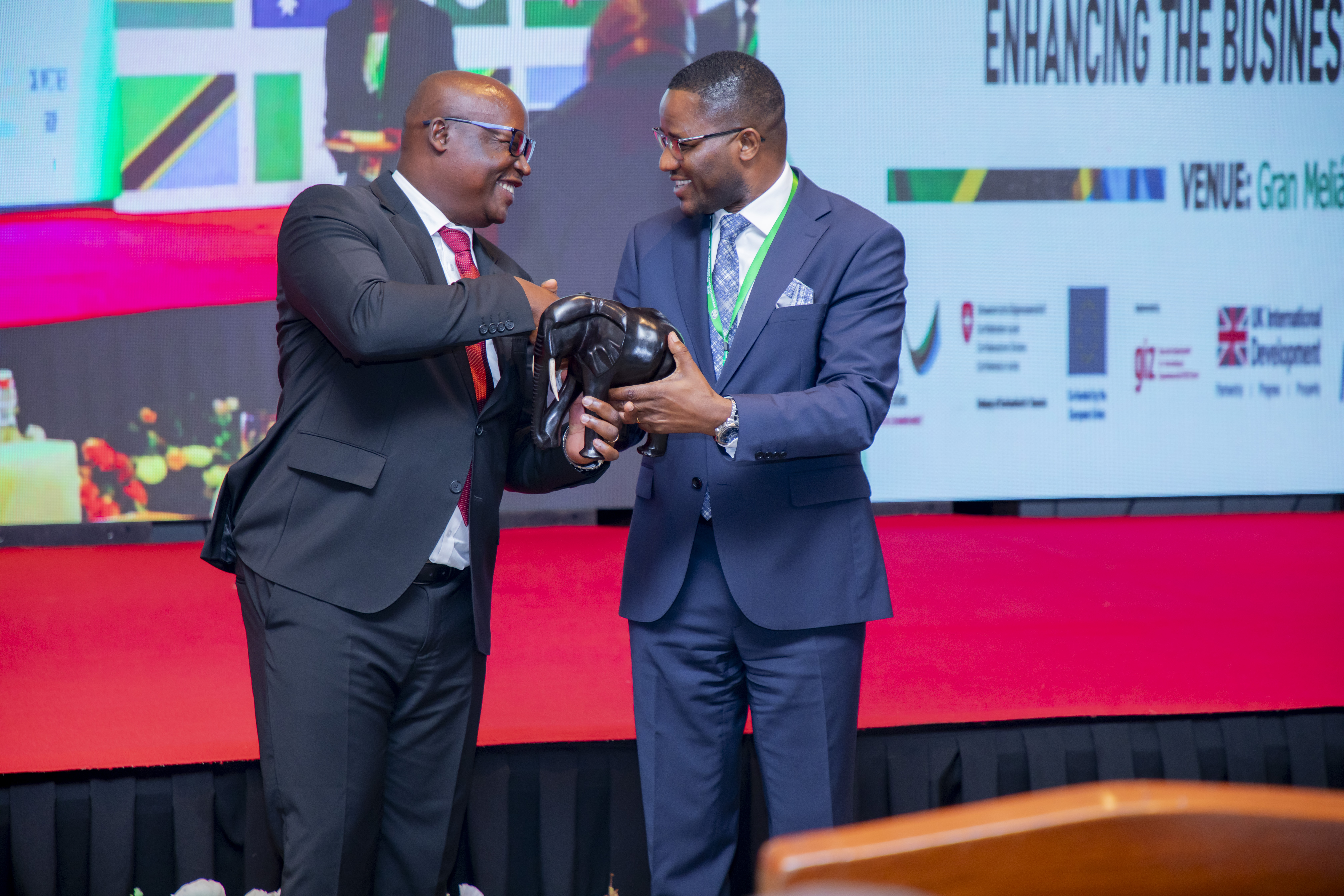 Msuluhishi wa Malalamiko na Taarifa za Kodi, Bw. Erastus Mtui, akimkabidhi Mheshimiwa Dennis Londo, Naibu Waziri wa Viwanda na Biashara wa Jamhuri ya Muungano wa Tanzania, zawadi ya kutambua mchango wake katika Mkutano wa Masuala ya Usuluhishi (Tanzania Ombudsman Forum 2026), uliofanyika tarehe 7–8 Septemba 2026 katika Hoteli ya Gran Meliá, jijini Arusha.